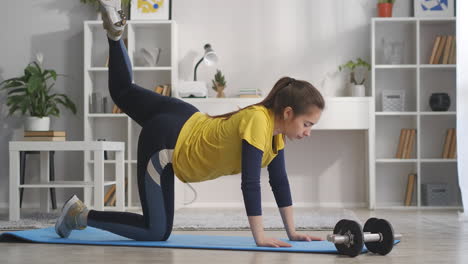 athletic-teenager-girl-is-training-at-home-alone-lifting-leg-up-tensing-muscles-home-fitness-and-healthy-lifestyle-standing-on-sport-mat-in-room